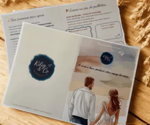 Le kit voyages de noces déposé sur une table en bois. On y voit la couverture avec un couple de dos se tenant la main et une page d'activité du kit.
